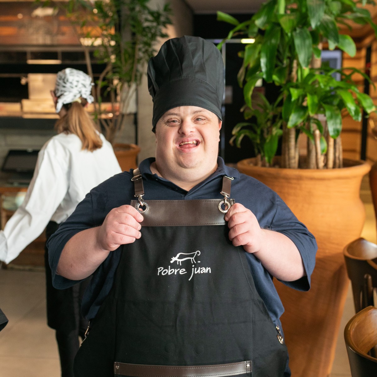 Participante do Pertence uniformizado no restaurante onde trabalha, sorrindo para a câmera.