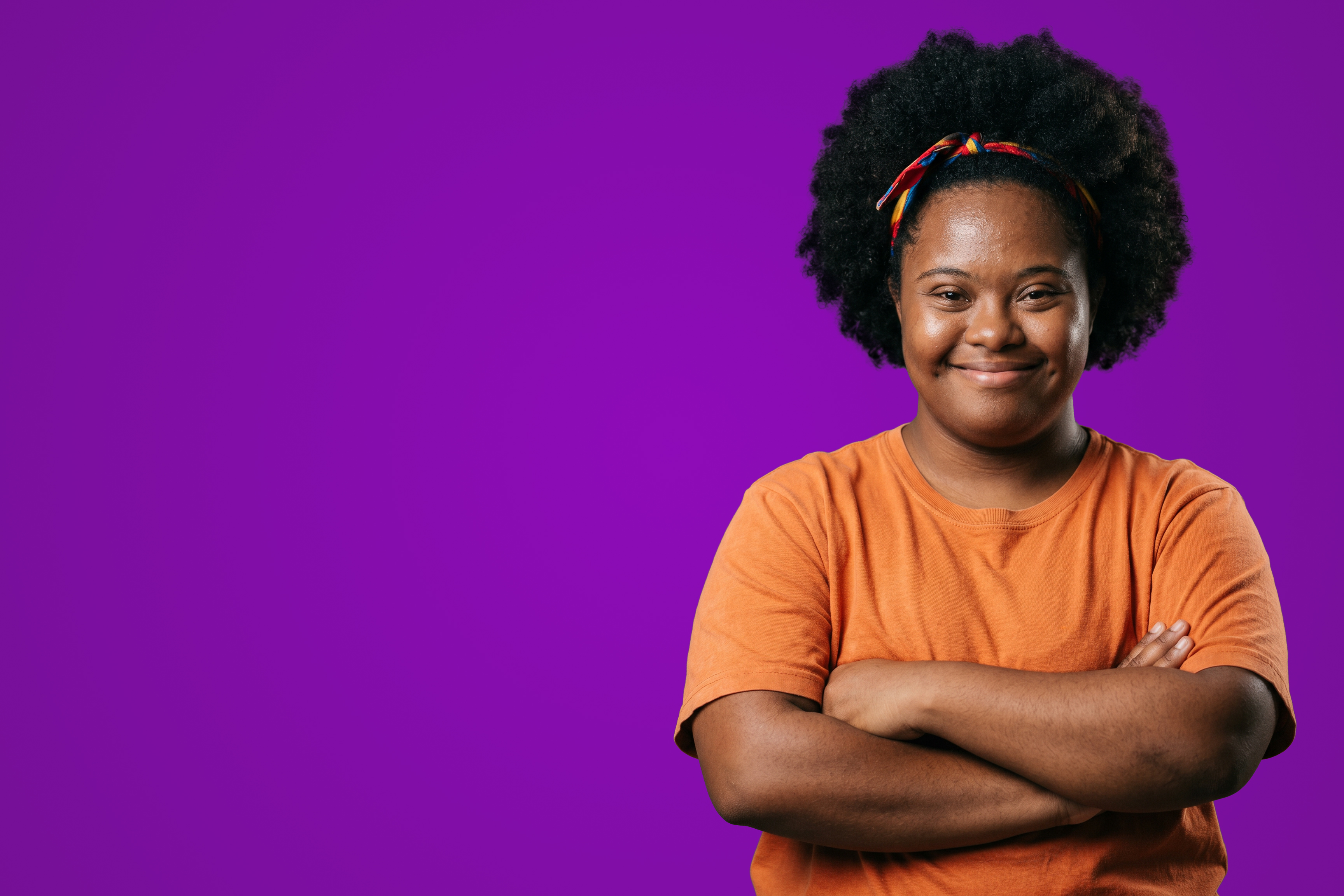 Jovem com síndrome de Down de braços cruzados, sorrindo com confiança.