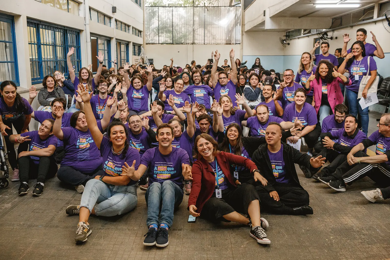 Equipe e participantes do Pertence reunidos, de camiseta roxa, acenando para a foto.